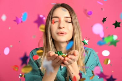 Happy woman blowing confetti on pink background
