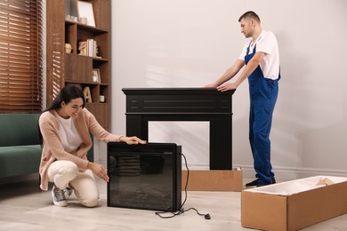 Young woman and professional technician with electric fireplace in room. Installing heater