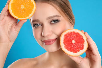 Young woman with cut grapefruit and orange on blue background. Vitamin rich food