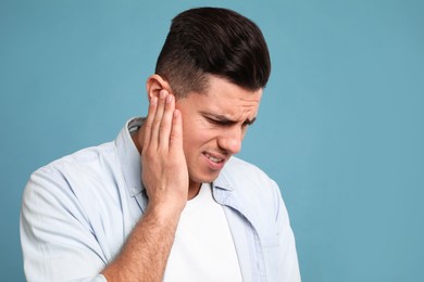 Photo of Man suffering from ear pain on light blue background. Space for text