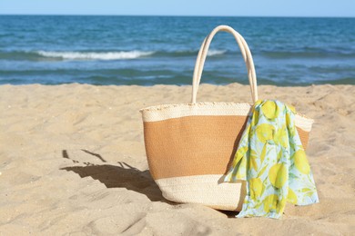 Straw bag with beach wrap on sandy seashore, space for text. Summer accessories