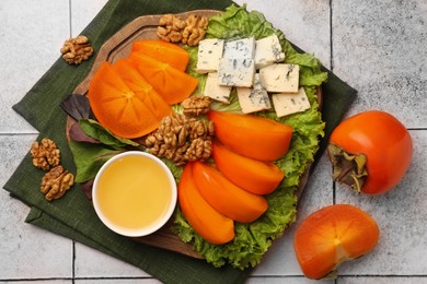 Photo of Delicious persimmon, blue cheese, nuts and honey served on tiled surface, flat lay