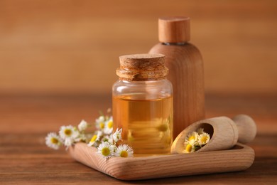 Bottles of chamomile essential oil and flowers on wooden table
