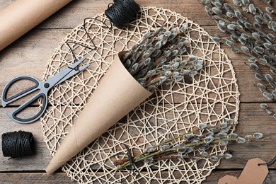Beautiful bouquet of pussy willow branches and wrapping materials on wooden table, flat lay