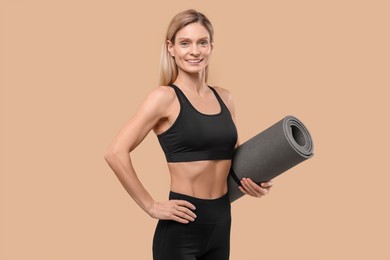 Photo of Athletic woman with fitness mat on beige background