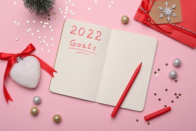 Planning goals for 2022 New Year. Notebook and festive decor on pink background, flat lay