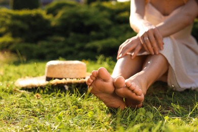 Woman sitting barefoot on green grass outdoors, closeup. Space for text