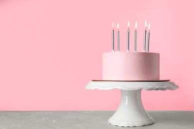 Birthday cake with burning candles on table against pink background, space for text