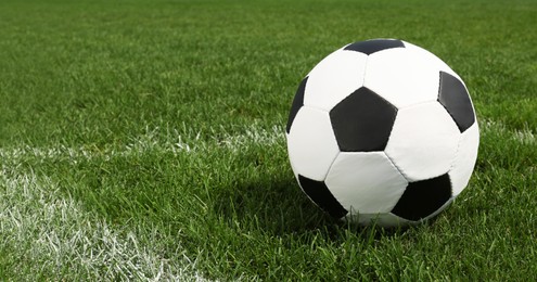Football ball on green field grass outdoors. Space for text