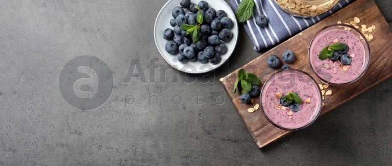 Glasses of tasty blueberry smoothie with oatmeal on dark grey table, flat lay with space for text. Banner design