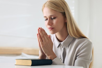 Religious young woman with Bible praying at home