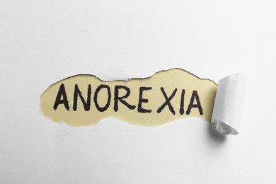 Word Anorexia written on beige background, view through hole in white paper