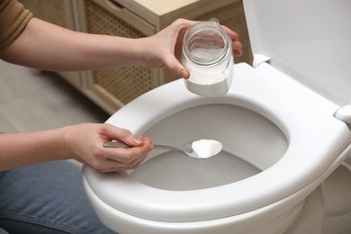 Photo of Woman cleaning toilet bowl with baking soda, indoors closeup
