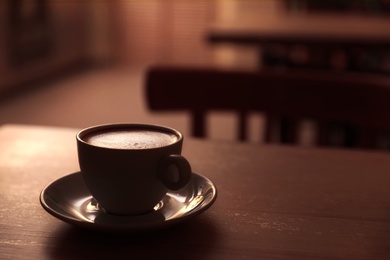Cup of fresh aromatic coffee on table against blurred background. Space for text