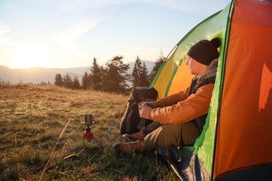 Man with cup of hot drink in camping tent. Space for text