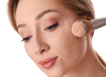 Beautiful young woman applying face powder with brush on white background, closeup