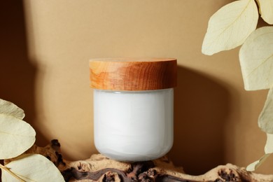 Jar of luxury cream and dried leaves on dark beige background
