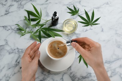 Top view of woman dripping THC tincture or CBD oil into coffee at white marble table, closeup