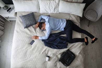 Exhausted businessman in office wear sleeping on bed at home after work, above view