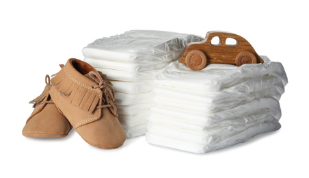 Disposable diapers, toy car and child's shoes on white background
