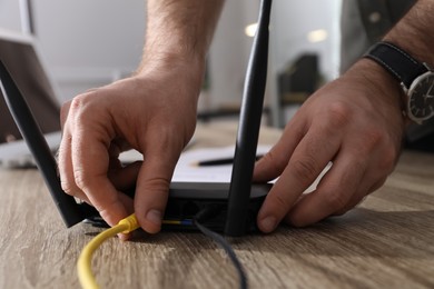 Man connecting cable to router at wooden table indoors, closeup. Wireless internet communication