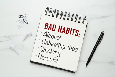 Notebook with list of bad habits and pen on white marble table, flat lay. Change your lifestyle