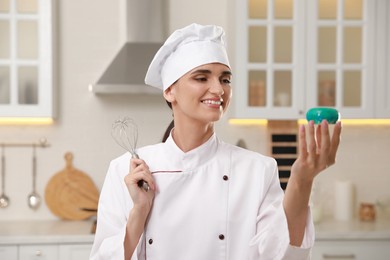 Photo of Happy professional confectioner with delicious cake and whisk in kitchen