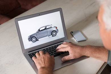 Man using laptop to buy car at wooden table indoors, closeup