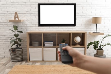Photo of Young man switching channels on TV set with remote control at home, closeup