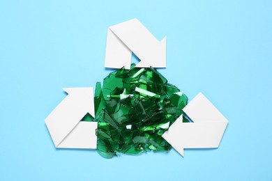 Photo of Recycling symbol and glass pieces on light blue background, flat lay
