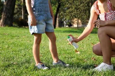 Mother applying insect repellent onto girl's leg in park, closeup