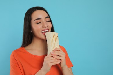 Photo of Young woman eating tasty shawarma on turquoise background. Space for text
