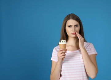 Emotional young woman with sensitive teeth and ice cream on color background. Space for text