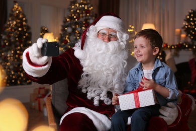 Santa Claus and little boy taking selfie in room decorated for Christmas