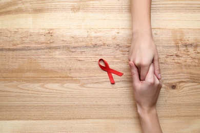 Women holding hands near red awareness ribbon on wooden background, top view with space for text. World AIDS disease day