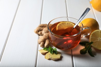 Photo of Cup of delicious ginger tea and ingredients on white wooden table, space for text