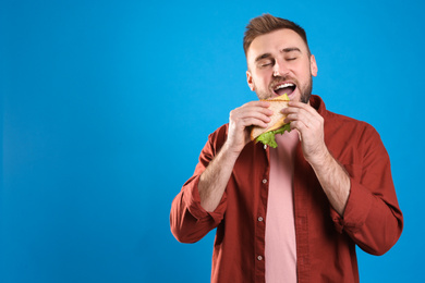 Photo of Young man eating tasty sandwich on light blue background. Space for text