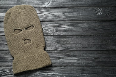 Photo of Beige knitted balaclava on black wooden table, top view. Space for text
