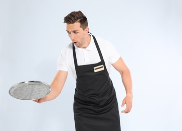 Clumsy waiter dropping empty tray on light background
