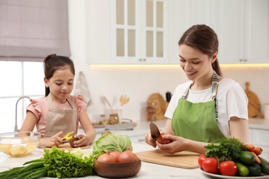 Mother and daughter peeling vegetables at table in kitchen