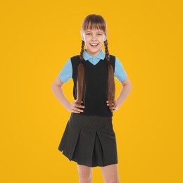 Portrait of cute girl wearing school uniform on yellow background