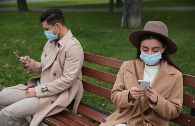 Man and woman using smartphones in park. Keeping social distance during coronavirus pandemic