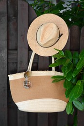 Stylish bag with hat and sunglasses hanging on wooden fence outdoors. Beach accessories