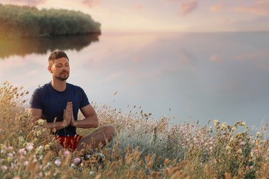 Man meditating in meadow near river. Space for text