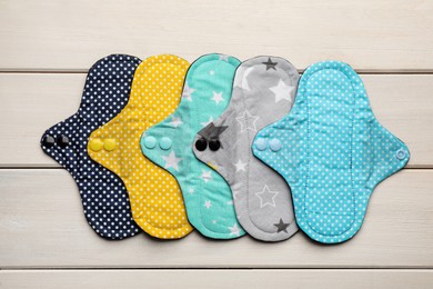 Many reusable cloth menstrual pads on white wooden table, flat lay