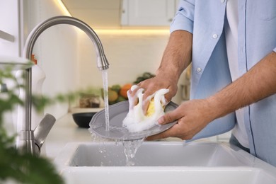 Man washing plate above sink in kitchen, closeup