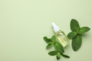 Bottle of essential oil and mint on light green background, flat lay. Space for text