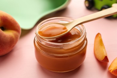 Photo of Spoon with healthy baby food over glass jar on pink wooden table, closeup