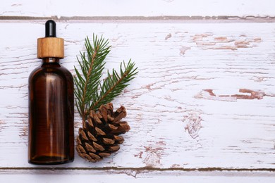 Bottle of pine essential oil, conifer tree branch and cone on white wooden table, top view. Space for text