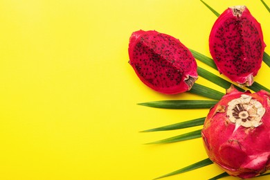 Delicious cut and whole red pitahaya fruits with palm leaf on yellow background, flat lay. Space for text
